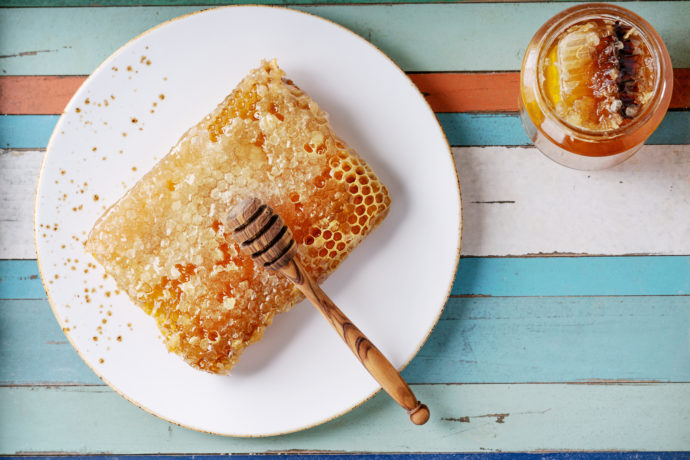 Honey with honeycomb and wooden dipper over wooden background. Top view